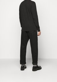 Top nero a maniche lunghe con dettaglio sulla cucitura posteriore, abbinato a pantaloni neri larghi e scarpe nere, con polsini arrotolati e suole spesse.