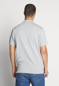 Grå bomullspolo med korta ärmar, en standardkrage och en slät textur. Bakvy visar en enkel, otyglad design.