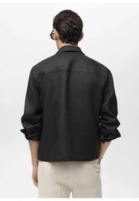 Black linen shirt with a collared neckline, rolled-up sleeves, and a straight cut. Minimalistic design with a smooth texture.