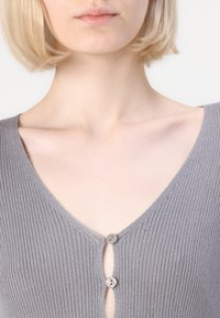 Gray knit top with a v-neckline and two buttons at the center. Texture is ribbed; fabric appears soft and lightweight.