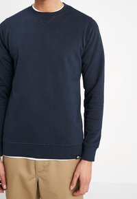 Laivastonsininen pehmeästä kankaasta valmistettu collegepaita, jossa on pyöreä pääntie, resorit hihansuissa ja helmassa, sekä pieni merkitty tagi alareunassa.