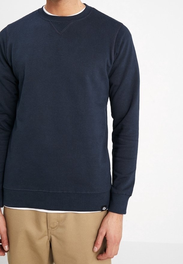 Laivastonsininen pehmeästä kankaasta valmistettu collegepaita, jossa on pyöreä pääntie, resorit hihansuissa ja helmassa, sekä pieni merkitty tagi alareunassa.