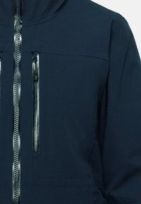 Navy blue jacket made of soft fabric, featuring a zippered front and two zippered chest pockets with reflective accents.