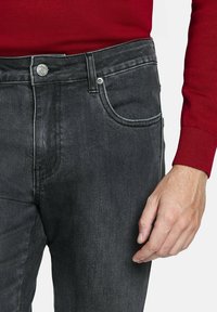 Jeans de mezclilla negra con un corte recto, que presentan un diseño clásico de cinco bolsillos y detalles de costura sutiles. Cierre de botón metálico en la cintura.