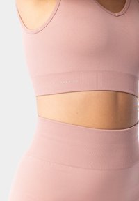 Světle růžový sportovní podprsenka s texturovaným povrchem, s širokým žebrovaným pásem a jemným logem, navržena pro pohodlí a podporu.