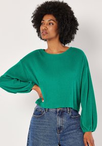 Grön ribbad stickad tröja med bred rund halsringning och ballongärmar, tillsammans med högmidjade blå denimjeans.