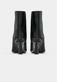 Botas negras hasta el tobillo hechas de un material suave con cierre de cremallera, que presentan un tacón esculpido y la marca DKNY en la suela.