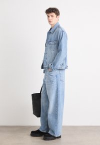 Light blue denim jacket and wide-leg jeans, paired with black platform shoes. The figure holds a black tote bag. Minimalist design, relaxed fit.
