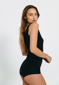 Sort tank top med en tætsiddende form og brede stropper, parret med matchende shorts, præsenteret mod en ensfarvet hvid baggrund.