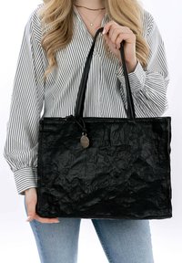 Borsa a spalla nera, screpolata, con manici doppi e un'etichetta in metallo. Texture liscia, forma rettangolare e una leggera lucentezza.