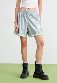 Silver satin athletic shorts with mint green stripes, elastic waistband, and front logo. Paired with black lace-up combat boots.