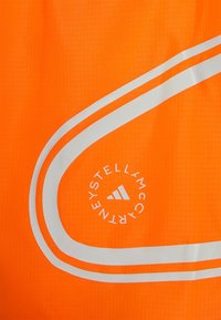 Tessuto arancione brillante con due strisce bianche riflettenti curve e un logo circolare che recita "Stella McCartney" intorno all'emblema Adidas.