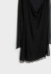 Robe longue noire à manches longues en chiffon transparent, à encolure drapée et ourlet asymétrique, suspendue devant un fond blanc.