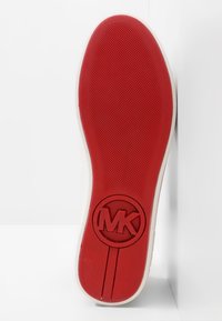 Semelle en caoutchouc rouge avec une prise texturée, logo circulaire MK au centre, côté de couleur crème. Finition lisse, forme légèrement arrondie.