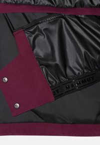 Skarlet och svart isolerad jacka med vattentät foder, utrustad med en stor ficka och märkeselastik vid fållen.