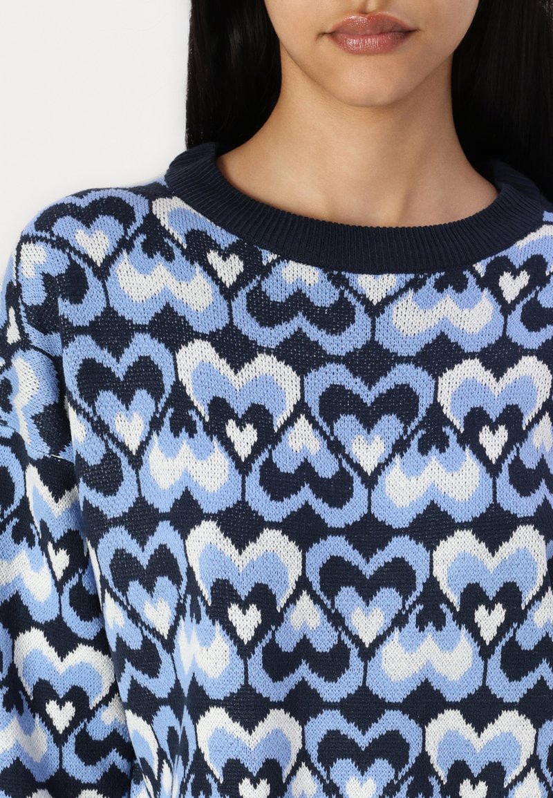Gebreide trui met een patroon van harten in tinten blauw, marineblauw en wit, met een geribbelde marineblauwe ronde hals en een gestructureerde stof.