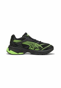 Zapatilla deportiva negra con acentos verdes, parte superior de malla y suela acolchada. El diseño incluye líneas gráficas para un detalle adicional.