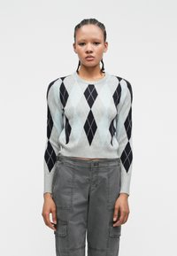 Pull en argyle gris et bleu clair, à manches longues et avec un col rond, associé à un pantalon cargo gris avec poches utilitaires.