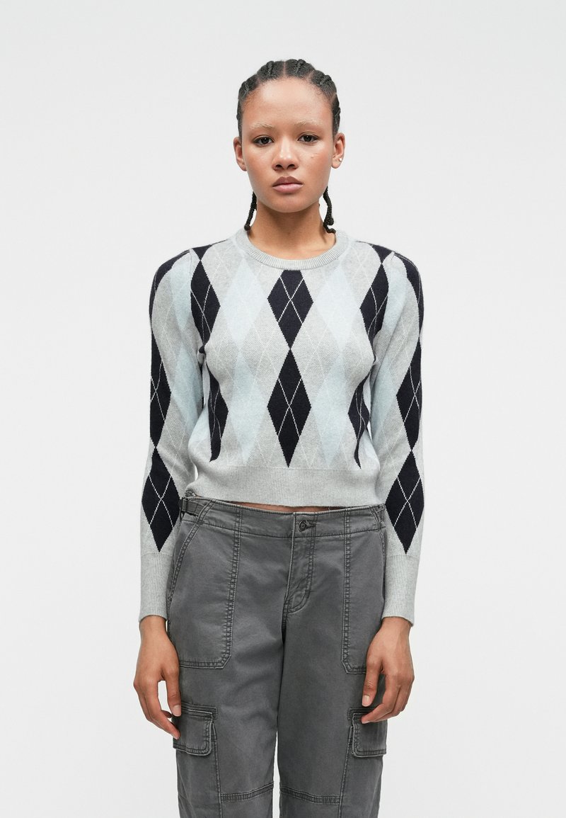 Pull en argyle gris et bleu clair, à manches longues et avec un col rond, associé à un pantalon cargo gris avec poches utilitaires.