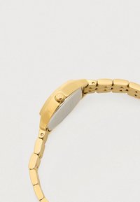 Gold wristwatch with linked metal band and smooth rounded case back, showing the side with adjustment crown on a light background.