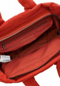 Red fabric tote bag interior with zippered pocket, textured lining, and a label. The bag features dual handles and a soft, structured design.