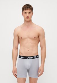Boxer shorts cinzentos da Nike com um cós elástico preto com o logótipo da Nike. O material é suave, com um design ajustado e pernas curtas.