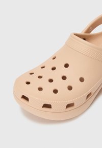 Light peach rubber clog with ventilation holes, textured strap, and a curved design. Notable accents include a raised grip along the sole.
