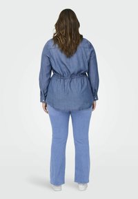 Denim srajca z dolgimi rokavi in elastičnim pasom, kombinirana z svetlo modrimi kavbojkami. Srajca ima ukrivljen rob in gumbe na zapestjih.