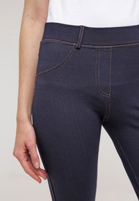 Mörkblå denimjeans med en figurnära design, med orange sömmar, framfickor och en slät yta. Medelhög midja.