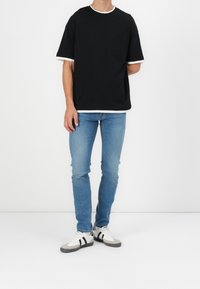 Czarny t-shirt z krótkim rękawem, z białym okrągłym dekoltem i mankietami, zestawiony z jasnoniebieskimi obcisłymi jeansami i białymi tenisówkami z czarnymi paskami.