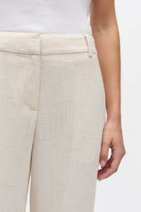 Beežid linased püksid, millel on sile tekstuur, sirge lõige, lame vöökoht ja taskud külgedel.