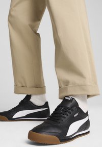 Svarta lädersneakers med vita accenter och en gummisula. Bärs med beige rullade byxor och vita strumpor. Gummiyttersula för bra grepp.