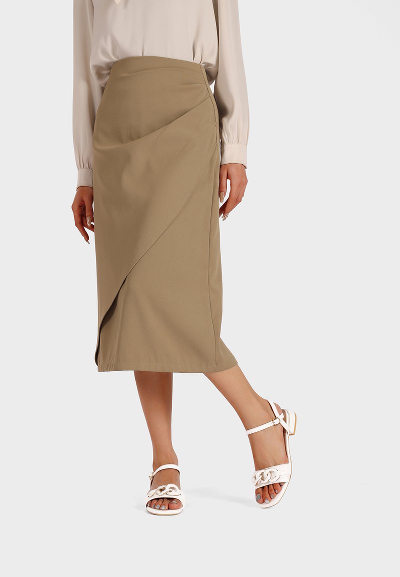 Gonna a matita khaki con design drappeggiato. Tessuto morbido, lunghezza al ginocchio, spacco laterale. Abbinata a sandali bianchi con accentuazione a catena.