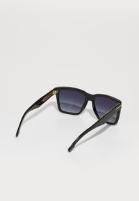 Óculos de sol pretos com um design retangular, apresentando lentes gradientes e hastes em destaque dourado com textura semelhante a madeira.