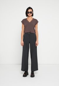 Camiseta marrón de cuello en V con ribete de encaje, combinada con pantalones grises de pierna ancha y cintura alta, y botas negras de plataforma con cordones.