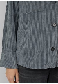 Gray corduroy jacket featuring vertical ribbed texture, button closure, and side pockets. Material is soft with a relaxed fit.