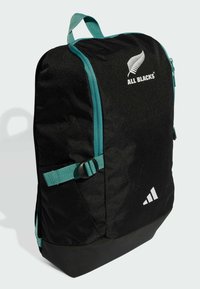 Schwarzer rechteckiger Rucksack mit türkisem Reißverschluss und Tragegurt, ausgestattet mit dem weißen "ALL BLACKS"-Logo und dem Adidas-Wappen auf der Vorderseite.