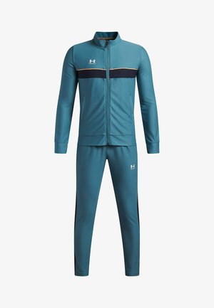 Ensemble de sport couleur bleu sarcelle en tissu lisse comprenant une veste zippée avec une bande marine et un pantalon avec des bandes latérales et un logo.