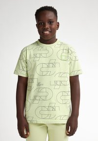 Groene T-shirt met korte mouwen, voorzien van zwarte geometrische patronen en een klein logo-patch op de borst. Gemaakt van zachte, lichte stof.