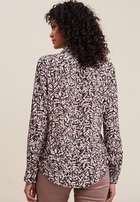 Blusa a maniche lunghe con un motivo di foglie nero e beige, realizzata in tessuto leggero, con orlo arrotondato e polsini con bottoni.