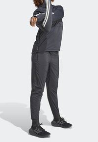 Zwarte sportjack met witte strepen, gecombineerd met bijpassende broek. De stof lijkt lichtgewicht, met een soepele textuur, ontworpen voor actieve kleding.