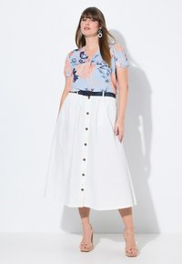 Witte button-up rok met zijzakken, gecombineerd met een blauw bloemen top met korte mouwen en een marineblauwe riem. Model draagt huidkleurige open hakken.