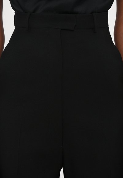 Black tailored trousers with a wide waistband, featuring a belt loop and a smooth, structured texture. Notable for clean lines and precision tailoring.