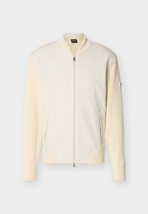 Veste bomber couleur crème avec manches en maille, fermeture éclair, col, poignets et ourlet côtelés, et poches latérales sur un fond uni.