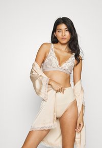 Bralett med blondedetaljer i beige, med V-halsdesign. Satengkåpe i lys beige med blondedetaljer. Høy midje nudefarget undertøy.