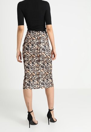 Haut noir côtelé associé à une jupe midi en satin imprimé léopard. Fente haute à l'arrière, texture lisse et silhouette ajustée avec des talons aiguilles.
