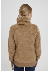 Tan fuzzy pullover med høj krave, elastiske manchetter og kant. Stofudtrykket ser blødt ud med en tekstureret finish, hvilket giver et hyggeligt udseende.