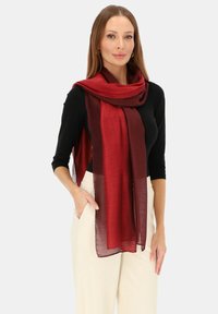 Szalik w kolorze burgunda i głębokiej czerwieni o gradiencie, wykonany z lekkiego, przezroczystego materiału, elegancko układający się wokół szyi na czarnej bluzce.