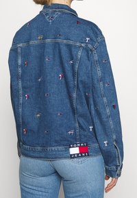 Spijkerjack in blauw met kleurrijke geborduurde logo's verspreid over het hele kledingstuk. Voorzien van een gebrandmerkte patch op de achterkant van de zoom en een klassiek kraagontwerp.