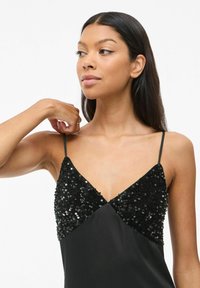 Vestido negro con un cuerpo de satén ajustado y un corpiño adornado con lentejuelas. Presenta finas tirantes y un diseño de escote en V.
